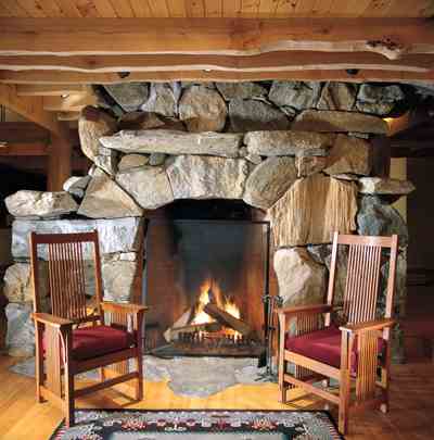 
The stone for the home’s six fireplaces and retaining walls was extracted on-site when the foundation and driveway were built. Designed for efficiency, the sides of this shallow, main floor fireplace curve inward. Five hundred feet of radiant tubing is coiled inside the stone to carry heat to the second floor. Most of the house has radiant floor heating, all connected to this central stone structure. The decor choices selected by the homeowner and his partner, an interior designer, harmoniously blend with the house design, recalling the synergistic pairing of Frank Lloyd Wright’s craftsmanship and love of Japanese design elements. Artfully intermingled with the Eastern influence are decidedly North American items such as the Teec Nos Pos Navajo rug and Stickley chairs pictured here.
